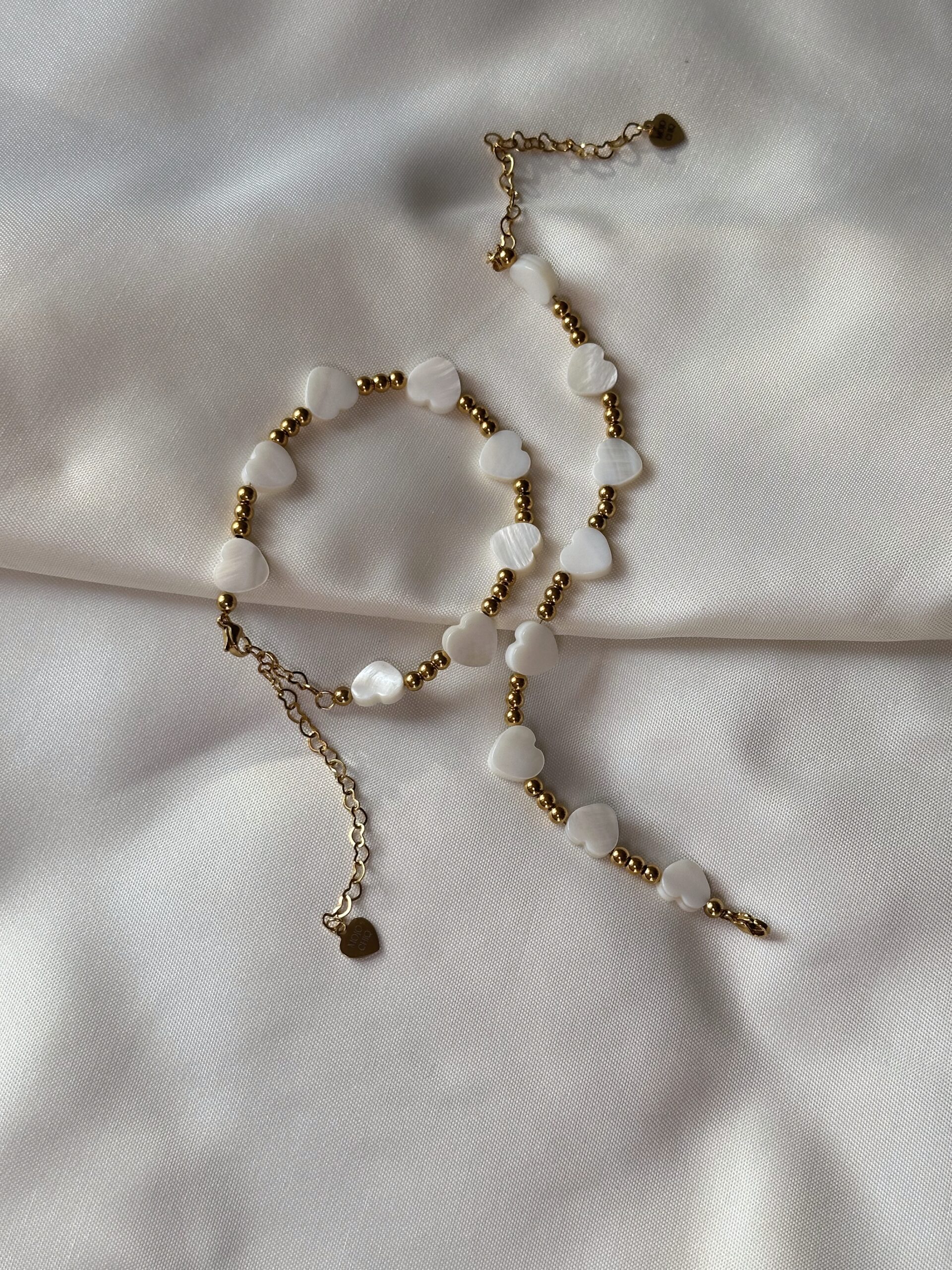 Oyster shell heart bead bracelet with 18K gold stainless steel spacers, adjustable chain, and heart charm, displayed on neutral-toned platform.